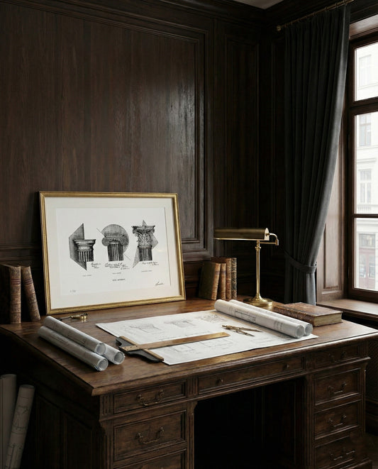 Stampa fine art "Ordo Aeternus" incorniciata in oro, posizionata su una scrivania da architetto con progetti, libri antichi e una lampada da tavolo in uno studio con libreria in legno scuro.