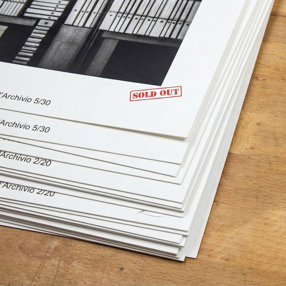 Dettaglio di una pila di stampe fine art in edizione limitata di Lorenzo Caia su tavolo di legno. La stampa superiore mostra un evidente timbro rosso "SOLD OUT" e la numerazione "Archivio 5/30", a dimostrazione dell'esclusività e dell'esaurimento delle serie.