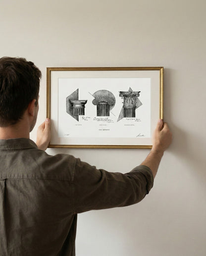 Persona che regge tra le mani l'opera "Ordo Aeternus" in formato A3 con cornice dorata. Riferimento visivo per le dimensioni reali della stampa architettonica appesa a parete.