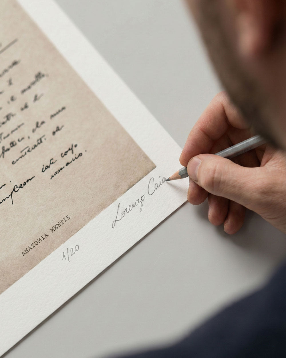 Dettaglio della mano dell'artista Lorenzo Caia mentre appone la firma autografa a matita e la numerazione 1/20 sulla stampa fine art "Anatomia Mentis". Garanzia di autenticità per collezionisti.